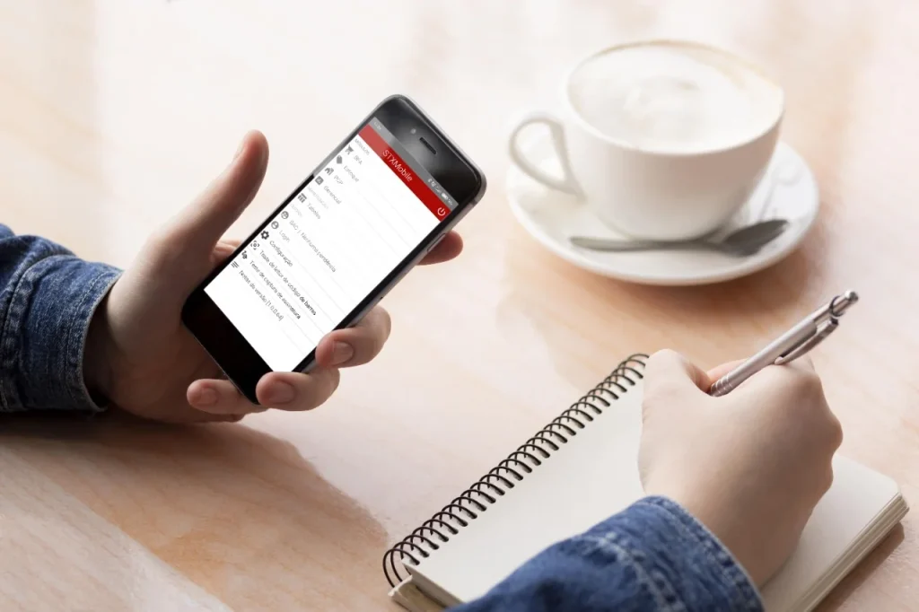 Vendedor consulta o menu do STX Mobile no celular enquanto anota em um caderno